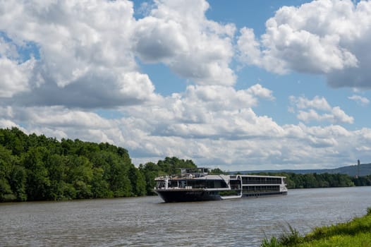 A pleasure boat sails along a river, with green nature, blue sky and white clouds