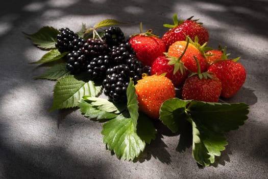 Strawberries and blackberries over dark background into natural sun light