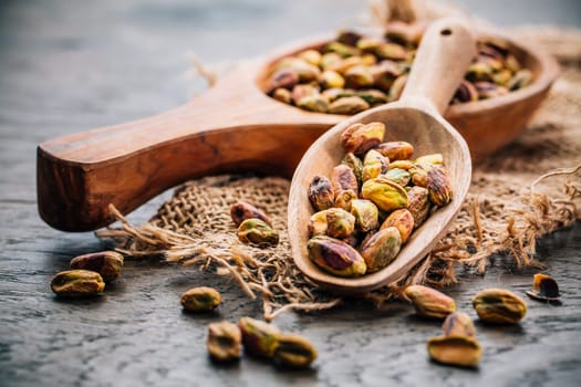 Roasted and peeled pistachios in wooden spoons on wooden background