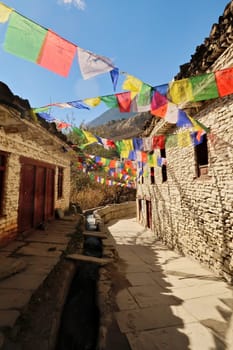 Many colorful buddhist prayer flags between traditional stone houses in the remote mountain village of Marpha, Annapurna Circuit Trek, Nepal 2022