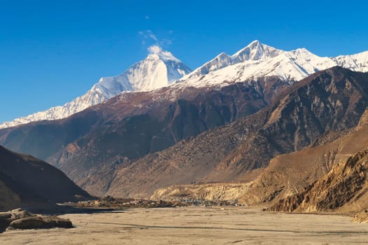The town, village of Jomsom behind the dried up riverbed of the Kali Gandaki River, the snow capped peak of Mount Dhaulagiri I rises in the background, Annapurna Circuit Trek, Nepal 2022