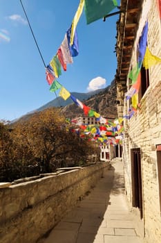 Many colorful buddhist prayer flags next to traditional stone houses in the remote mountain village of Marpha, Annapurna Circuit Trek, Nepal 2022