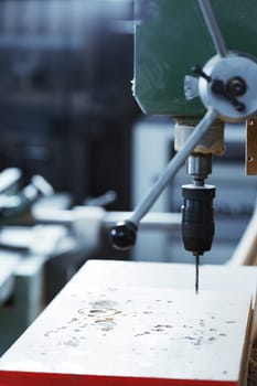 Powerful drill press is drilling through a white wooden plank in a professional workshop, creating perfectly round holes for a woodworking project