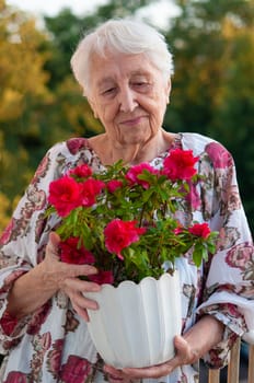 The senior old woman with flowers on the balcony at home
