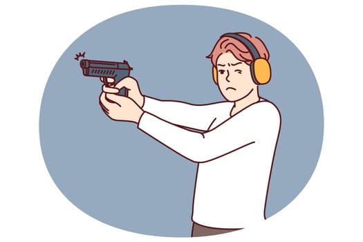 Man with gun trains at shooting range to learn how to shoot and become sheriff or bodyguard. Guy in ballistic headphones holds gun and squints to hit target during training in shooting range
