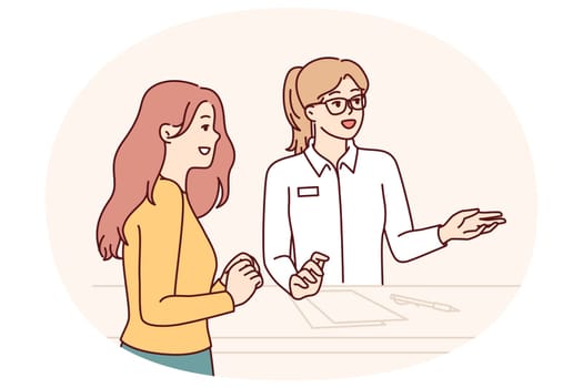 Woman working at reception in hotel or beauty salon consults client, helps to choose beautician and best procedure. Girl visiting cosmetology clinic stands near reception with administrator