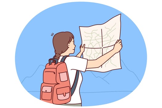 Woman tourist looks at map choosing route for trip through wild during hike in mountainous area. Girl tourist with backpack behind back studies map of national park and enjoys journey