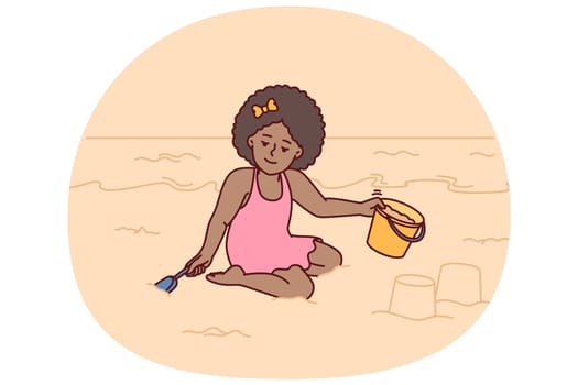 Little girl playing with sand sitting on beach building castle with bucket and shovel during summer holidays at resort. Pre-teenage girl located on sea beach relaxing alone on sea or ocean