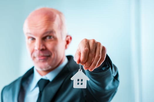 Businessman in a suit holds a house keychain, symbolizing real estate and financial security. Perfect for business designs