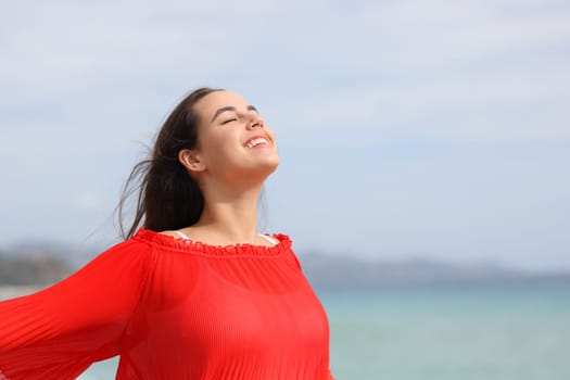 Happy woman in red breathing fresh air on the beach