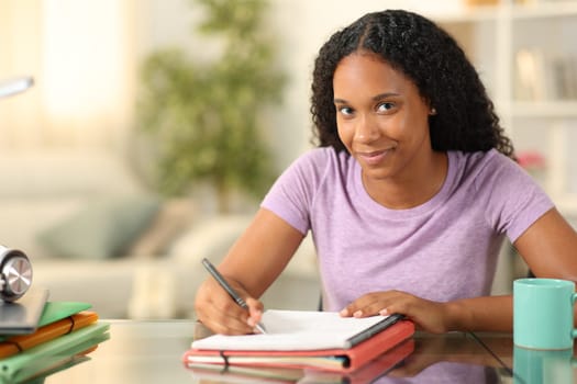 Proud black student looking at you learning taking notes at home