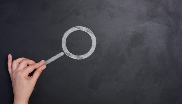 A woman's hand and a magnifying glass drawn with white chalk on a black chalk board, searching.