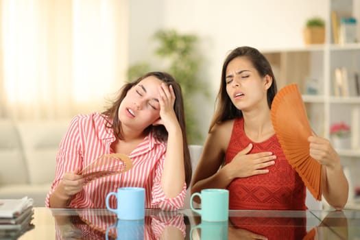 Front view of two stressed roommates fanning suffering heat stroke at home