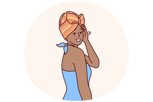 Charming African American woman with traditional turban on head is dressed in blue dress for going to ethnic party. African girl smiling and looking at screen demonstrating fashion national minorities