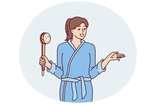 Woman in bathrobe holding shower brush in hand going to take bath and do self bodycare or anti-aging treatments. Positive girl after shower points to side, drawing your attention to importance hygiene