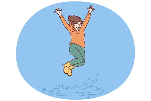Happy woman jumping in puddle enjoying first autumn rain after hot summer. Girl in good mood in casual clothes jumps standing in puddle, receiving positive emotions from long-awaited walk