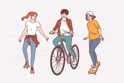 Summer walk of cheerful friends using rollerblades and bicycle or skateboard for recreation. Walk through park of teenage boys and girls enjoying friendship or opportunity to communicate with peers