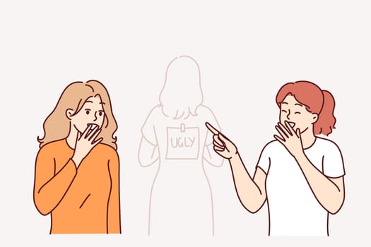 Girls laugh at classmate with ugly written on back, for concept of bullying and shaming in schools. Problem of teenage shaming among students who want to assert themselves at expense of other children