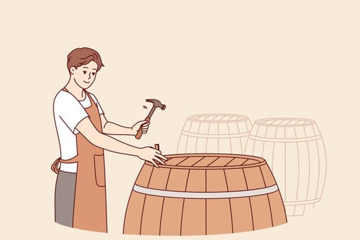 Man winemaker opens barrel with finished drink to taste bordeaux made from organic grapes. Guy is standing in wine cellar, hammering barrel of sherdane to infuse and impart unique smell to wine.