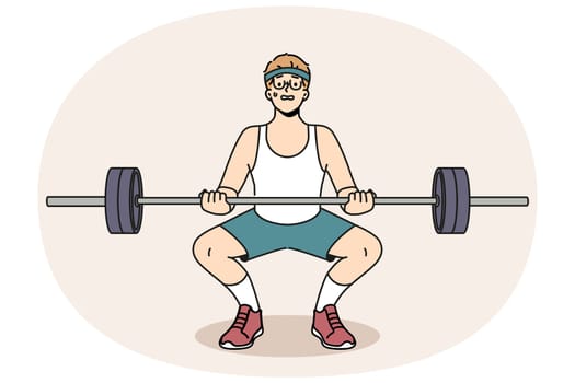 Man with barbell goes in for sports in gym, wanting to have beautiful figure and healthy body. Guy novice bodybuilder squats with barbell in hands and needs help of fitness trainer.