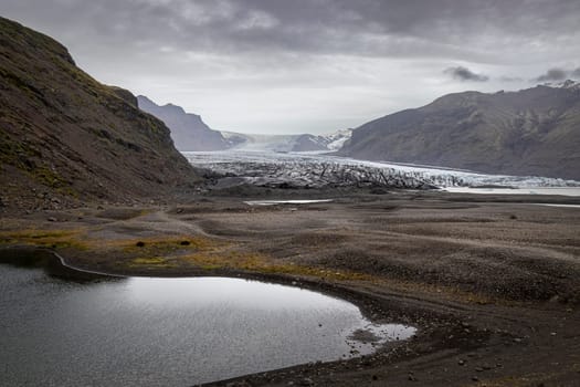 Vatnajokull Glacier Svinafellsjokull Small lake reflecting cloudy sky Iceland