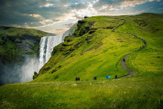 Tourists enjoying  beautiful day hiking up  path  skogafoss waterfall iceland