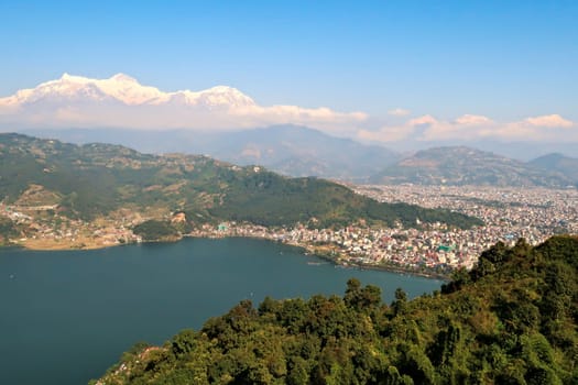 View onto the town of Pokhara at the shore of Phewa Lake, a mountain range with Mount Machapuchare on the left rising in the back, on the way up to the World Peace Pagoda, Nepal 2022