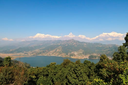 View onto Phewa Lake in front of a mountain range with Machapuchare in the middle, on the way up to the World Peace Pagoda close to Pokhara, Nepal 2022