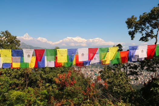 View onto the mountains rising behind the Phewa Lake, Machapuchare on the left, colorful prayer flags in the foreground, on the way up to the World Peace Pagoda, Pokhara, Nepal 2022
