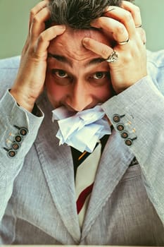 Stressed businessman stuffing mouth with paper to cope with pressure and responsibility
