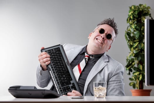 Manager with sunglasses holding a keyboard while drinking alcohol and smiling, hiding alcoholism and feigning courage at the office issues of alcoholism in the workplace