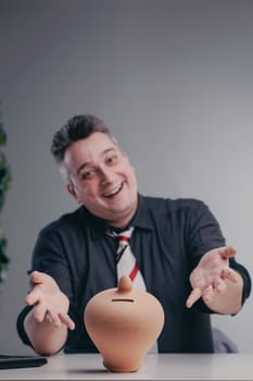Businessman is smiling and showing an empty piggy bank, suggesting a need for savings or highlighting a lack of funds