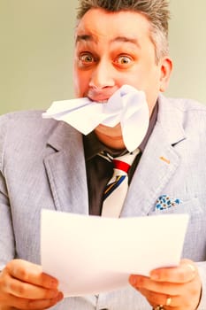 Overwhelmed businessman biting paper, shocked and worried, facing stress and burnout in corporate setting. Irony and satire of workplace emotions