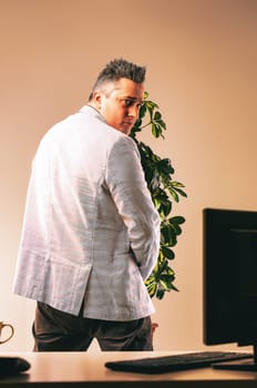 Manager hides behind a plant, peeking over his shoulder with a sneaky expression in an office, creating a negative workplace atmosphere