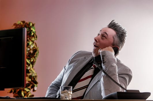 Businessman is talking on the phone at his desk, feigning cheerfulness while hiding his alcoholism issues of alcoholism in the workplace