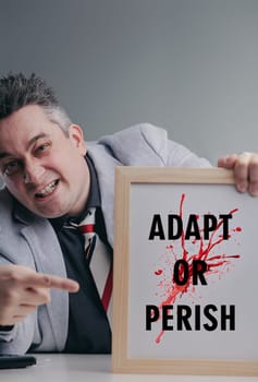 Businessman is pointing at a sign that says adapt or perish with a determined expression, emphasizing the need for adaptation in a competitive business environment