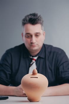 Worried businessman at his desk with an empty piggy bank, showing concern about finances. Stressful, thoughtful, and anxious in a corporate setting