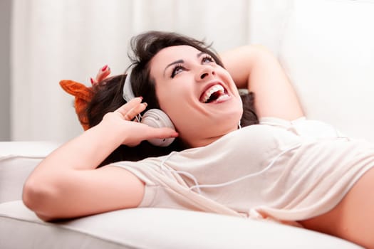Young woman is lying on her couch with her eyes closed, laughing and enjoying the music playing through her headphones