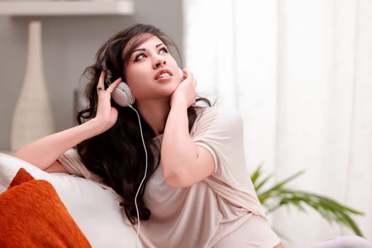 Young woman lounges on her cozy sofa at home, listening to music with headphones, looking happy and serene