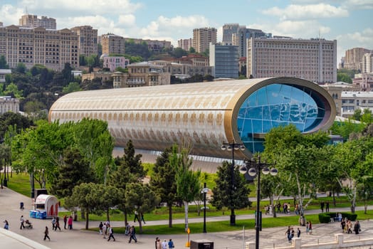 Baku, Azerbaijan - May 5, 2024: Visitors explore the unique architecture and exhibits of the Carpet Museum in Baku, surrounded by greenery and city life.