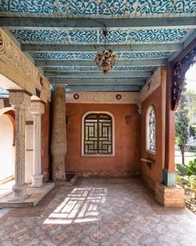 A serene courtyard showcases intricate ceiling designs, elegant pillars, and patterned flooring, illuminated by soft afternoon light