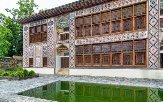 Intricate architecture of Shaki Khan's Palace, in Shaki, Azerbaijan, surrounded by lush greenery and a tranquil reflection pool.