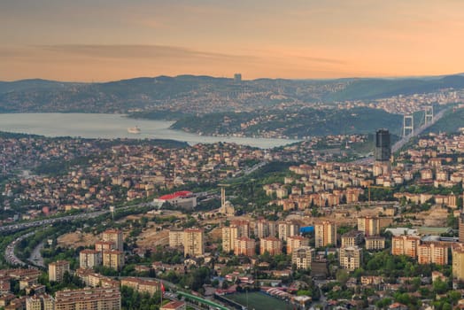 The urban skyline of Istanbul, Turkey is captured at sunset, showcasing sprawling neighborhoods, the Bosphorus Strait, and distant hills