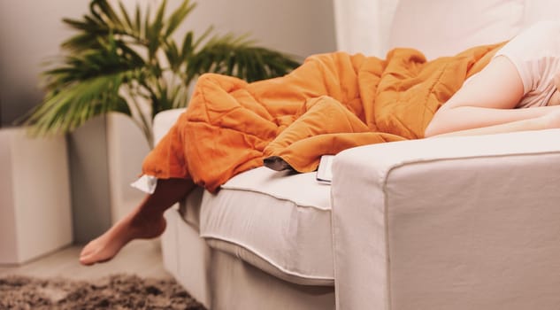 Lifestyle A woman is enjoying her quality time at home, taking a nap on the sofa, covered with a warm blanket