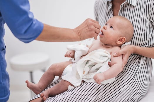 Pediatrician administring oral vaccination against rotavirus infection to little baby in presence of his mother. Children health care and disease prevention.