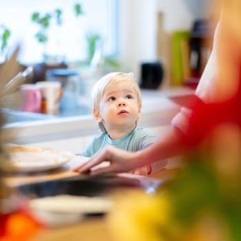 Mother and little toddler baby boy making pancakes for breakfast together in domestic kitchen. Family, lifestyle, domestic life, food, healthy eating and people concept