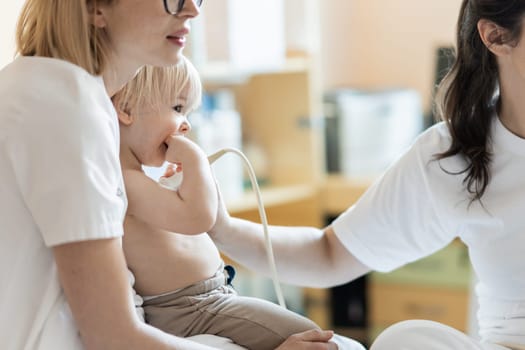 Small child being checked for heart murmur by heart ultrasound exam by cardiologist as part of regular medical checkout at pediatrician