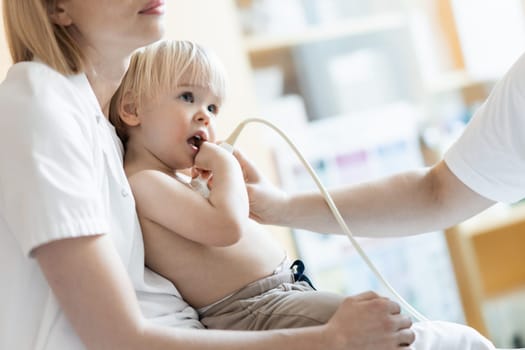 Small child being checked for heart murmur by heart ultrasound exam by cardiologist as part of regular medical checkout at pediatrician