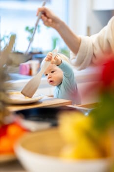 Mother and little toddler baby boy making pancakes for breakfast together in domestic kitchen. Family, lifestyle, domestic life, food, healthy eating and people concept