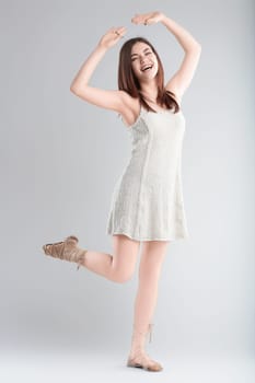 Young woman in a white dress dances joyfully in a studio, eyes closed, arms raised gracefully, exuding elegance and beauty